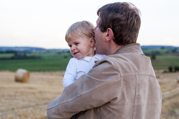 Fototapeta premium Young father and adorable little son hugging on straw field