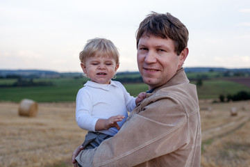 Fototapeta na wymiar Young father and adorable little son hugging on straw field