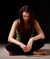 A young woman sitting on the floor, isolated on black background