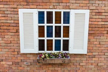 Fototapeta na wymiar White window frame on a red brick wall with flowers