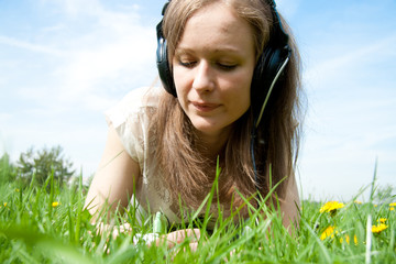 Beautiful young woman listening music laying in the grass
