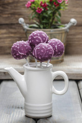 Purple cake pops in white ceramic pot on wooden background.