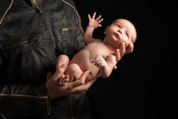 A father in a motorcyclist jacket holds his newborn son