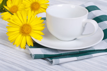 White cup and saucer with bouquet of daisies on a wooden table