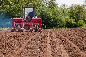 Obraz premium Old tractor with sower working on fields view from far down