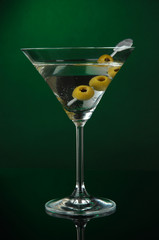 Martini glass with olives on dark green background