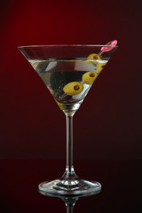 Martini glass with olives on dark red background