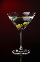 Martini glass with olives on dark red background