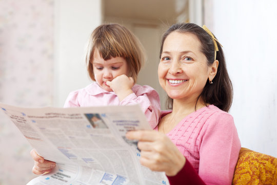 Mature woman and  girl reads newspaper