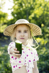 Young girl with cucumber in the garden