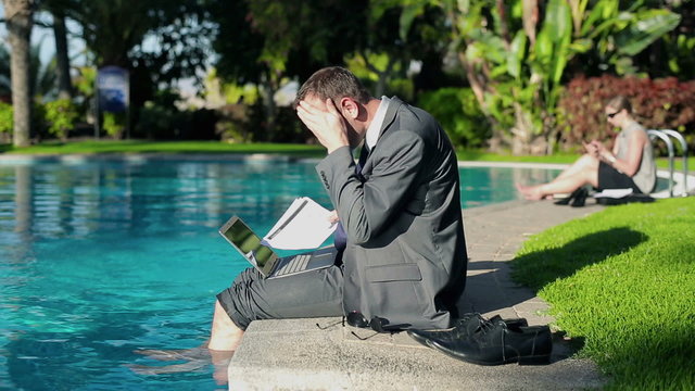 Businessman sitting by the poolside and getting bed news