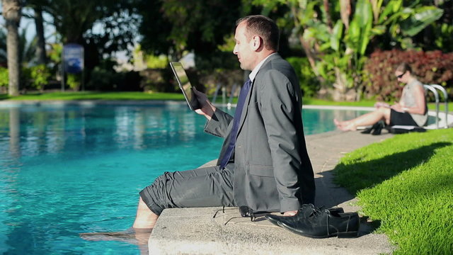 Businessman sitting by the poolside and chatting on tablet compu