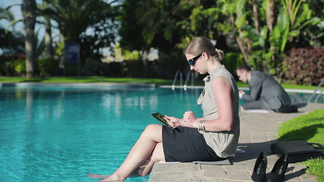 Businesswoman sitting by the poolside and working on tablet comp