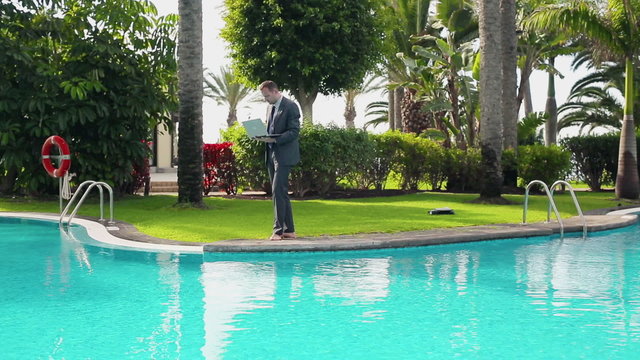 Businessman walking by the poolside and working on laptop comput