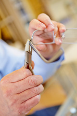 Hand mit Zange repariert Brille