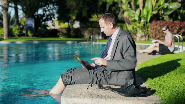 Businessman sitting by the poolside and working on tablet comput