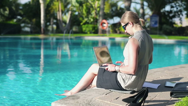 Businesswoman working on laptop computer by the poolside