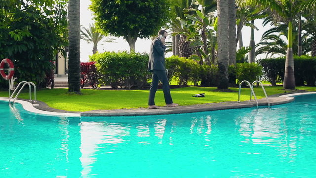 Businessman walking by the poolside with cellphone