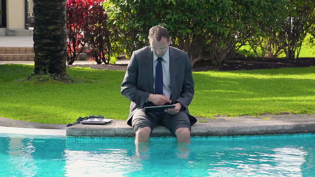 Businessman sitting by the poolside and working on tablet comput