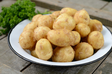 Young potato in metal bowl on wooden background