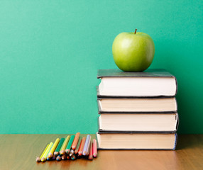 Green apple on a pile of books and pencils
