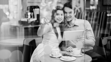 Happy couple in cafe holding digital tablet