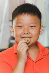 Young asian boy eats a piece of biscuit