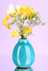 Beautiful bouquet of freesia in vase on purple background