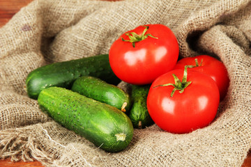 Tasty green cucumbers and red tomatoes on sackcloth background