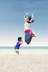Obraz premium Asian mother jumping with daughter at beach