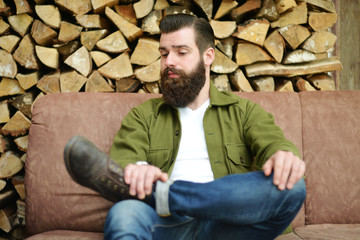 Men with beard sitting on a verranda with wood in the background