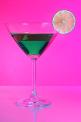Green cocktail in martini glass on pink background