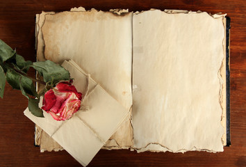 Open old book, letters and rose on wooden background