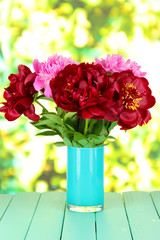 Beautiful peonies in vase on table on bright background