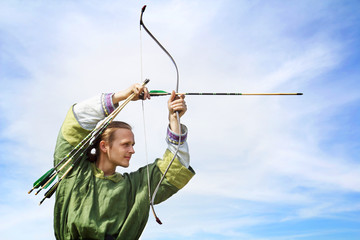 Young archer with bow and arrows in medieval costume aiming