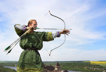 Young archer with bow and arrows in medieval costume aiming