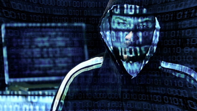 Hacker looking at the camera with laptop, binary codes projectio