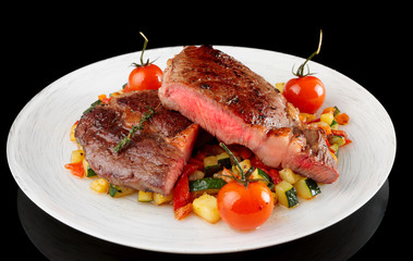 Medium fried steak with vegetables on black background