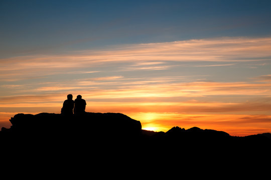 Couple having relax on top of a rock at sunset