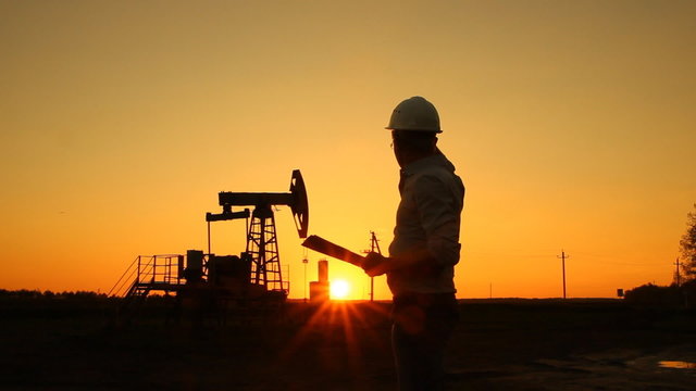 Man (engineer) with securities for the oil pumping unit. sunset 