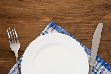 white plate, knife and fork on wood