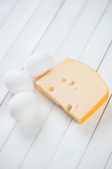 Vertical shot of chicken eggs and a slice of fresh cheese