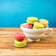 Macaroons in coffee cup on wooden table over blue background