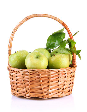 Juicy green apples with leaves in basket, isolated on white