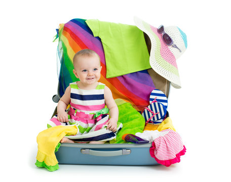 Baby girl sitting in suitcase with  things for vacation travel