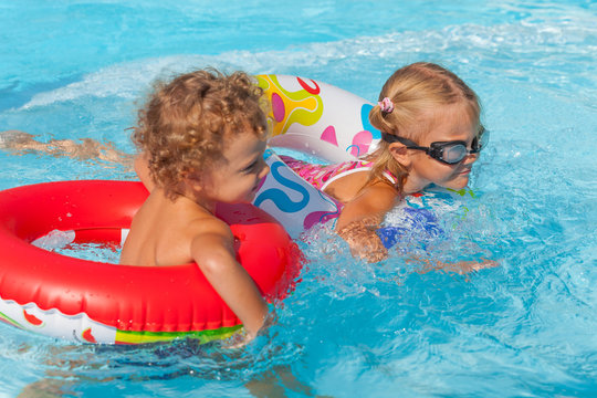 little girl and little boy playing in the pool with rubber rings