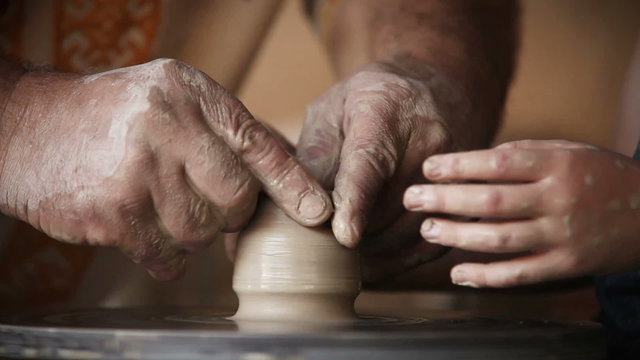 Hands of old potter and young pupil