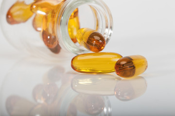 yellow vitamin capsules spilled out from jar on white