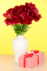 Beautiful peonies in vase on table on yellow background