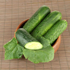 Tasty green cucumbers in wooden bowl, on bamboo mat background